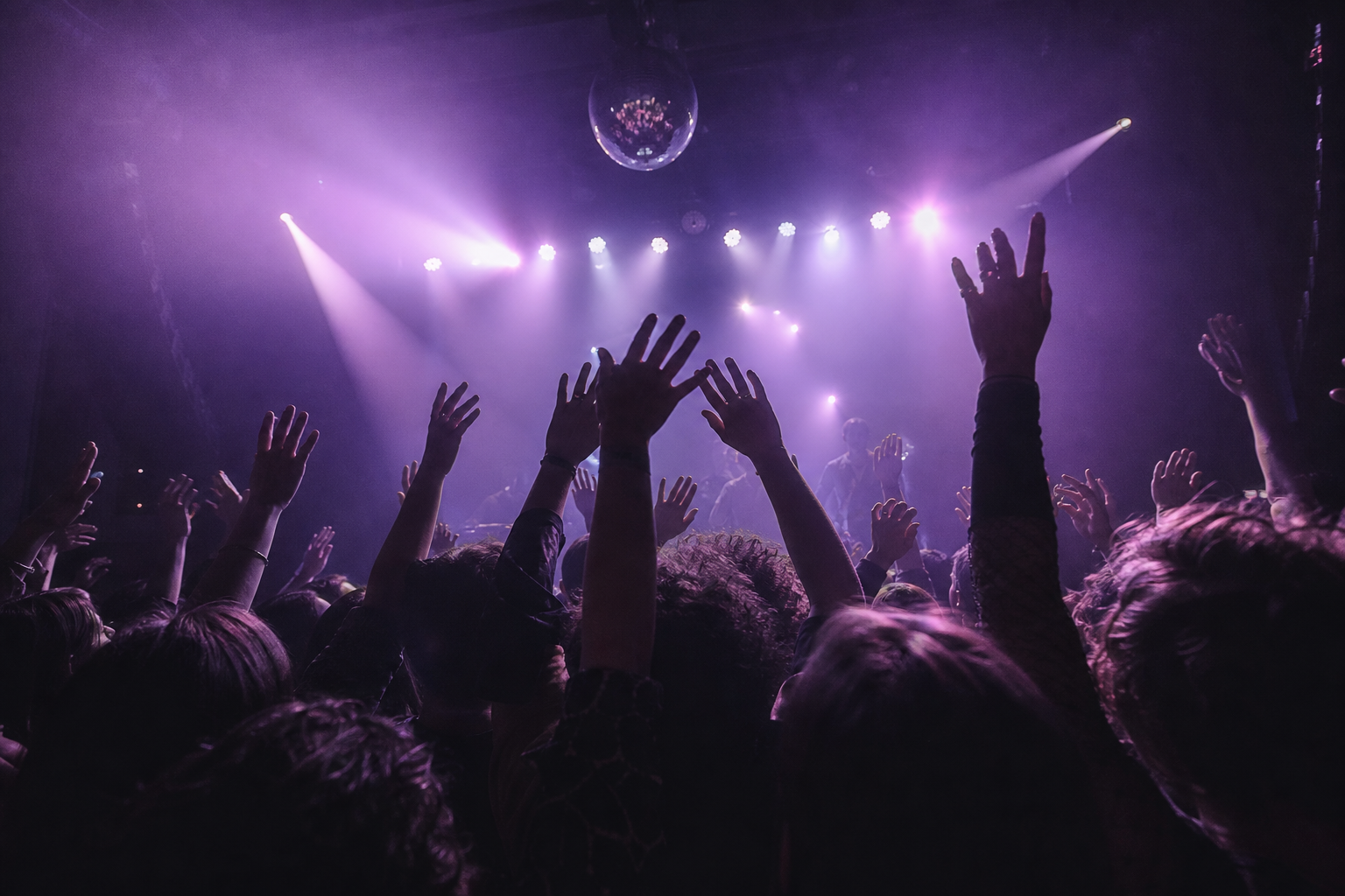 View from inside a crowd with hands raised toward the stage