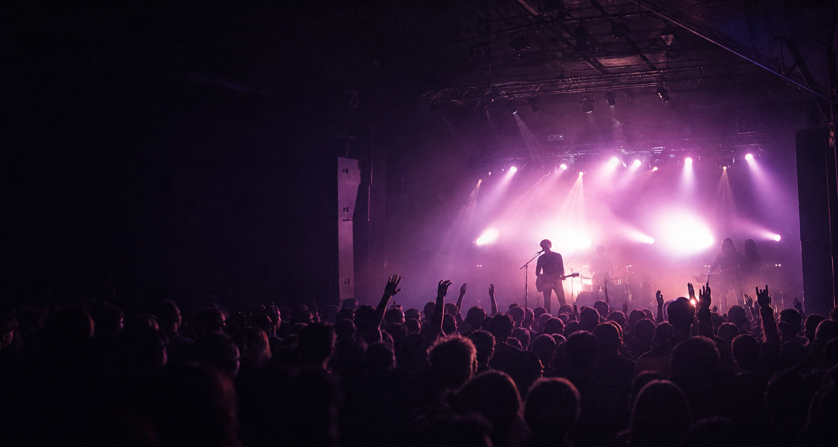 Wide view of the crowd and stage at a violet-lit concert